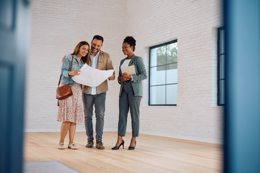 A joyful young couple and their professional advisor reviewing documents together during a successful home walkthrough.